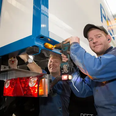 Technicus controleert en repareert achterlicht van een vrachtwagen in een werkplaats voor mobiliteit en techniek