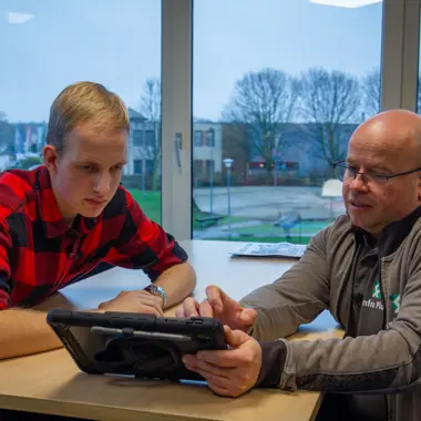 Een docent begeleidt een student bij het bestuderen van informatie op een tablet, gericht op groene opleidingen.