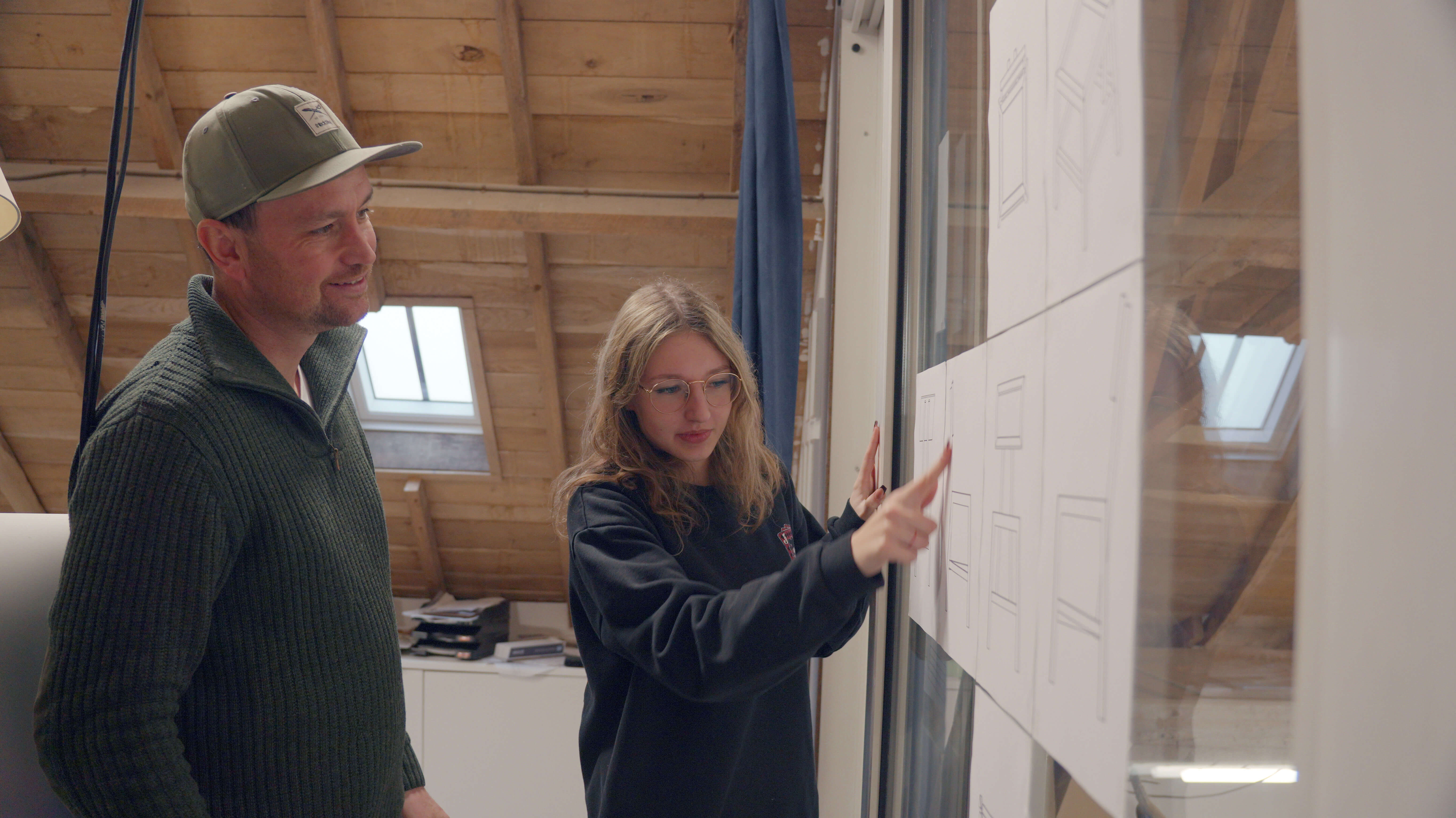 Student wijst uitleg aan op een groot document tijdens overleg met instructeur in een werkruimte.