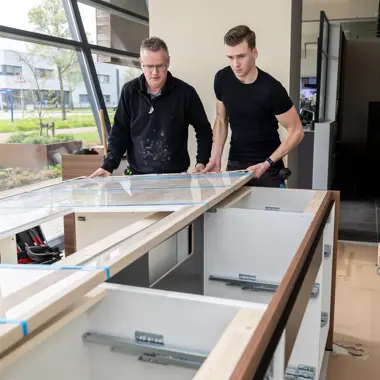 Twee personen richten een keukeninterieur in met moderne meubels en stijlvolle werkbladen.