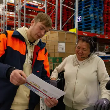 Medewerkers bespreken logistieke planning in magazijn vol pallets en dozen