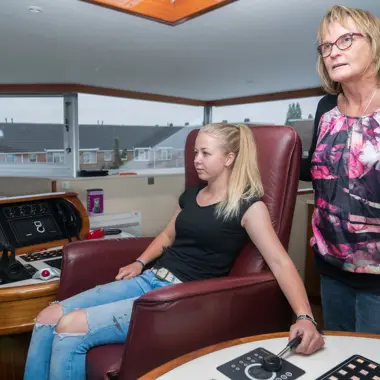 Jongere bestudeert navigatieapparatuur aan boord, begeleid door docent maritieme techniek.