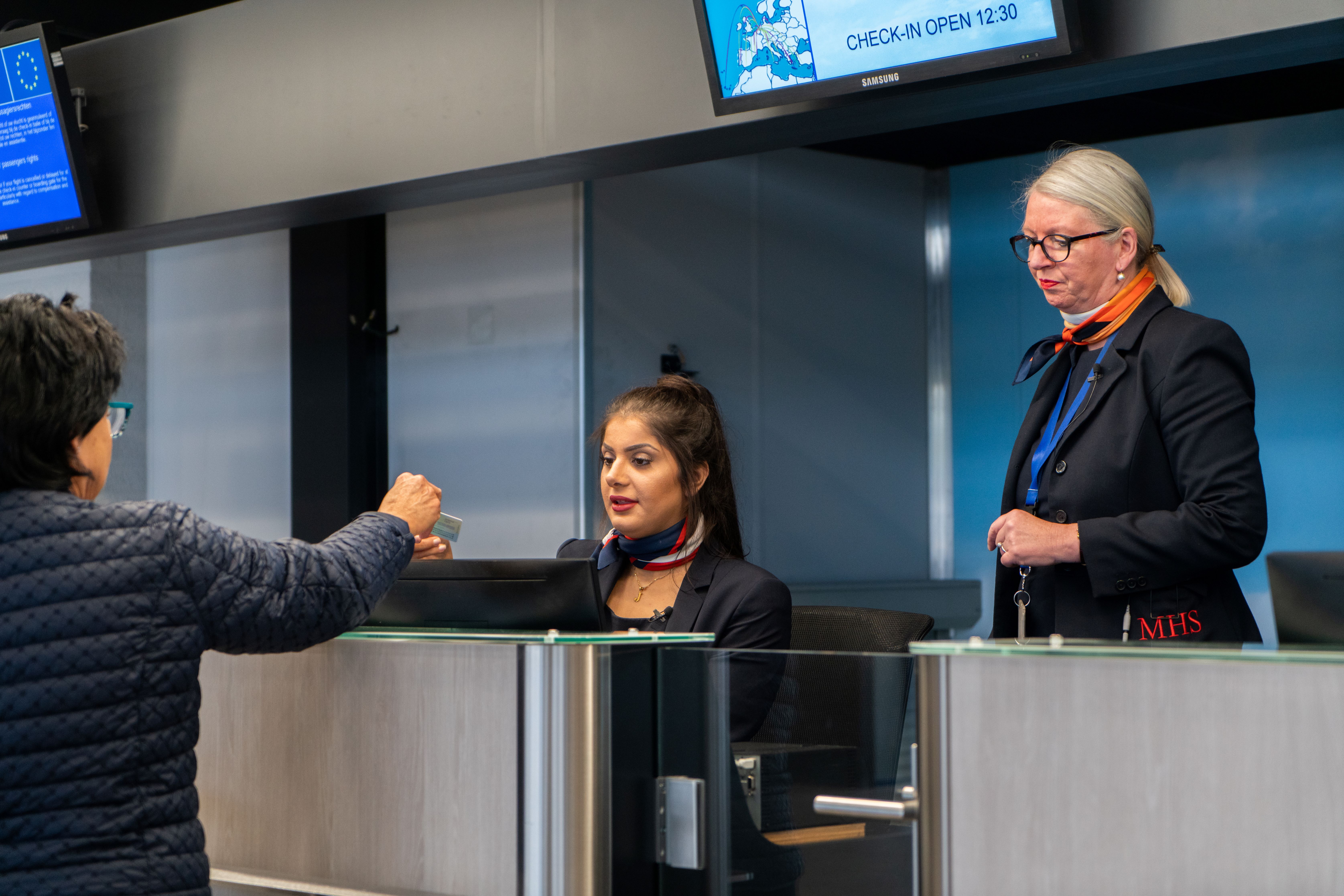 Luchtvaartdienstverleners begeleiden passagiers bij het inchecken en verzorgen servicebalie in een luchthavenomgeving.