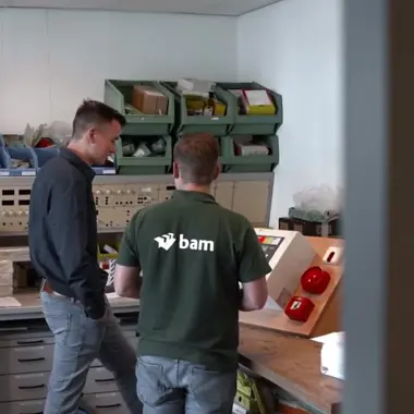 Twee technici bekijken een bedieningspaneel voor elektrische installaties in een werkplaats