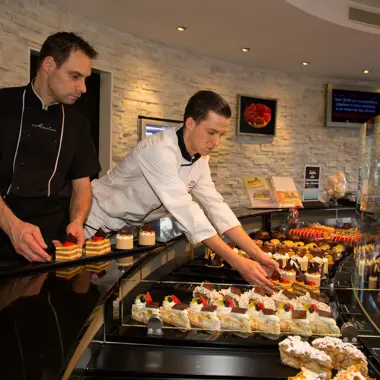 Leerlingen presenteren met zorg een assortiment gebak in een bakkerijwinkel voor presentatie en verkoop.