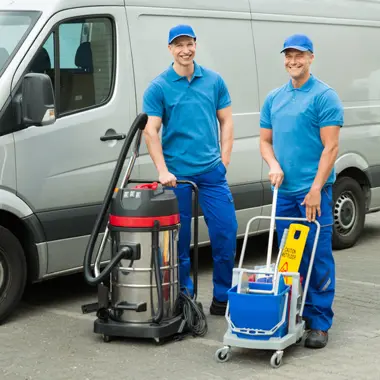 Twee schoonmakers poseren met schoonmaakapparatuur voor een bus op een parkeerterrein