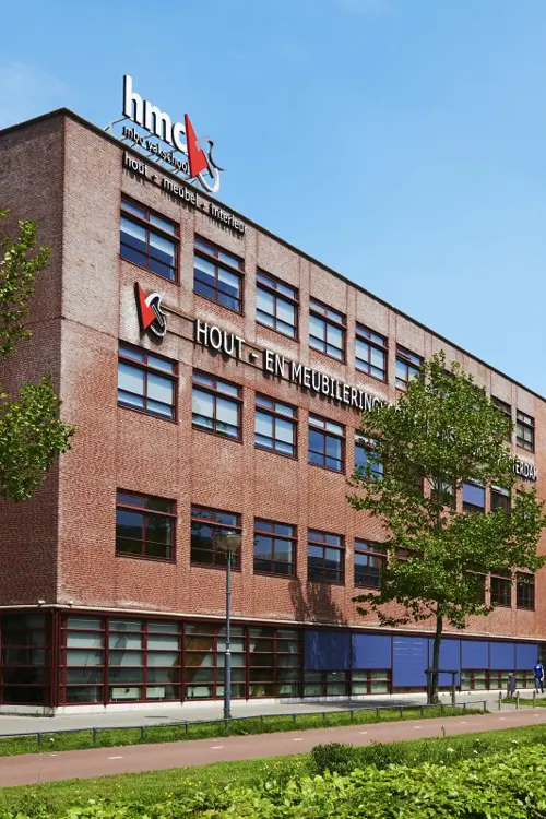 Het gebouw van Hout- en Meubileringscollege Amsterdam aan de Pieter Calandlaan met straat en groenvoorziening