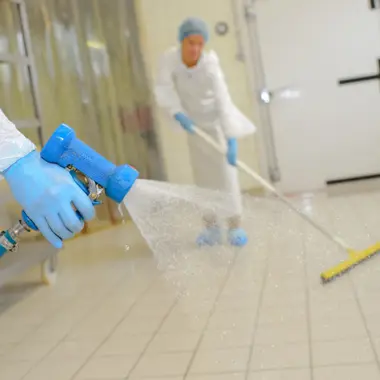 Medewerker reinigt tegelvloer grondig met waterstraal en dweil in professionele werkomgeving