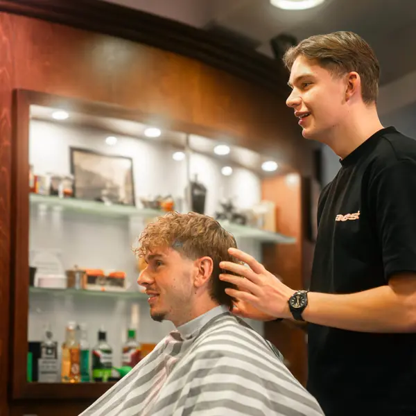 Leerling-kapper verzorgt en knipt het haar van een klant in een modern kapsalon tijdens een mbo-opleiding.