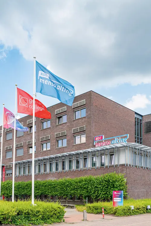 Hoofdgebouw van ROC Menso Alting in Groningen met vlaggen en een duidelijke ingang aan Gedempte Kattendiep.