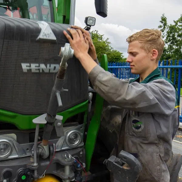 Technisch specialist onderzoekt en repareert een tractor, bezig met onderhoud aan motor en hydraulieksystemen