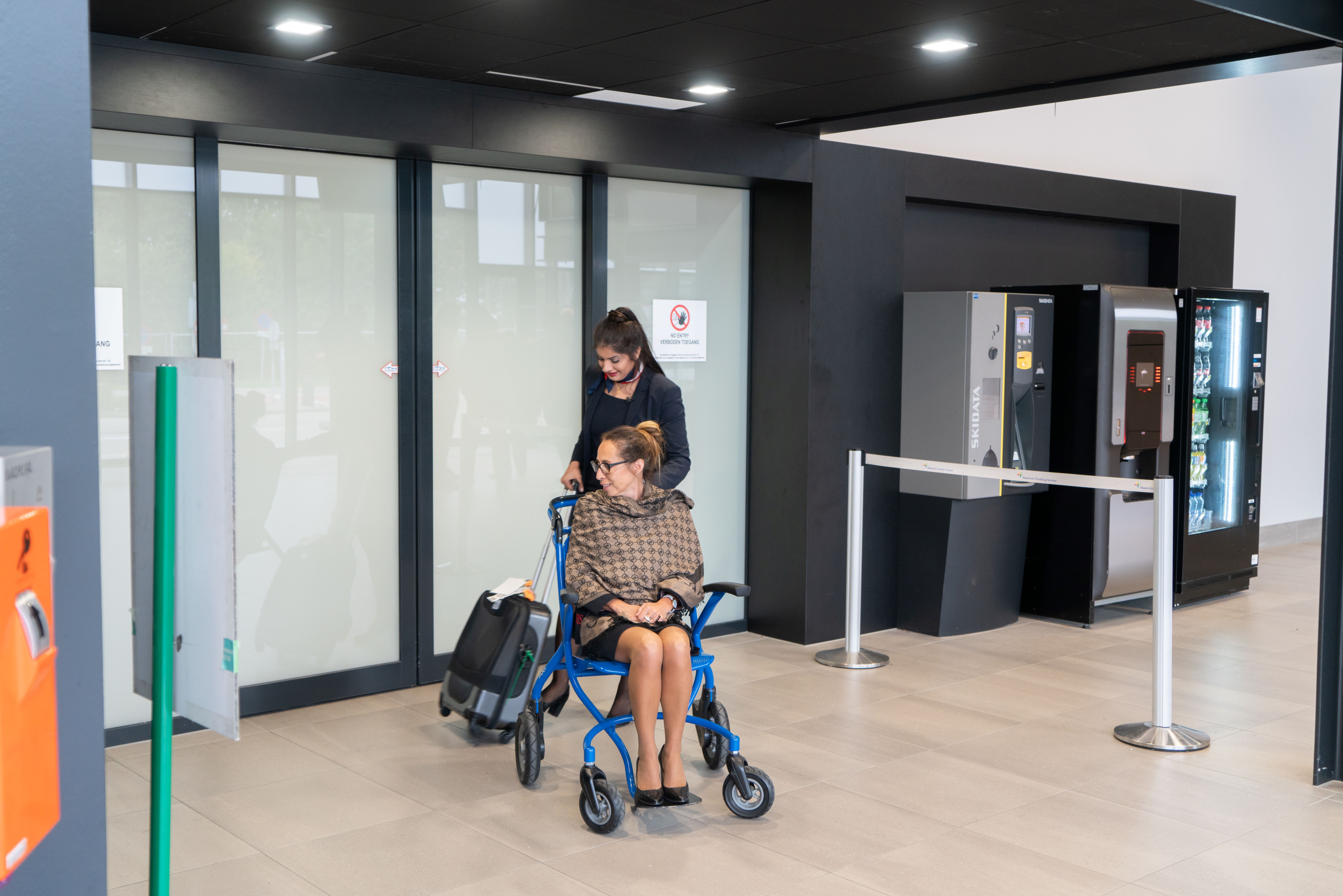 Luchtvaartdienstverlener begeleidt passagier in rolstoel in een luchthavenhal voor een comfortabele reis.