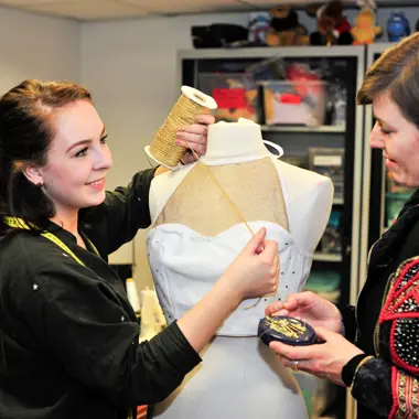 Twee modeprofessionals werken samen aan het ontwerpen en afpassen van een kledingstuk op een paspop in een atelier.
