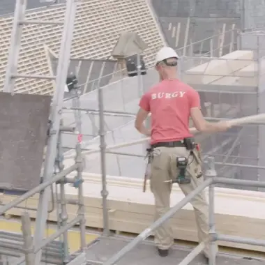 Vakbekwame bouwmedewerker werkt op steiger aan een woning in aanbouw.
