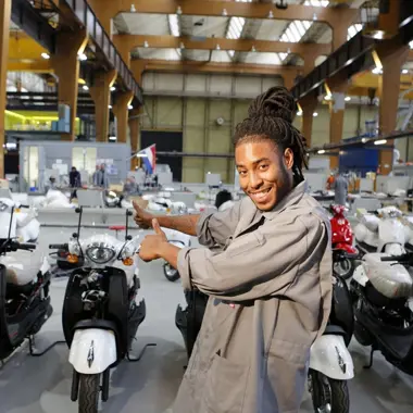 Assistent mobiliteitsbranche wijst enthousiast naar een rij elektrische scooters in een werkplaats
