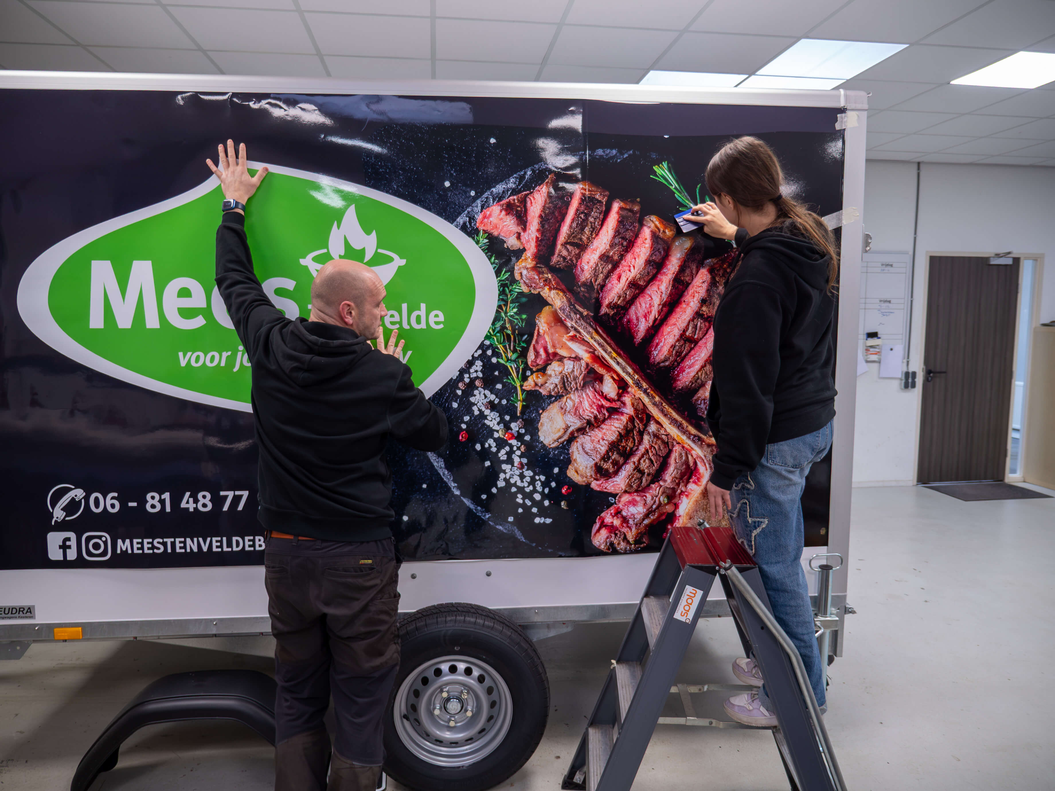 Bezoekers plakken een reclameposter met vlees en groenten op een vrachtwagenwand in een werkplaats