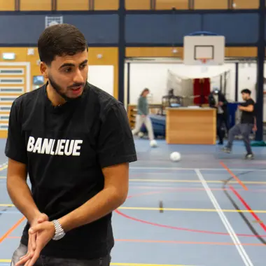 Begeleider ondersteunt jongeren bij een sportactiviteit in een gymzaal ter bevordering van welzijn.