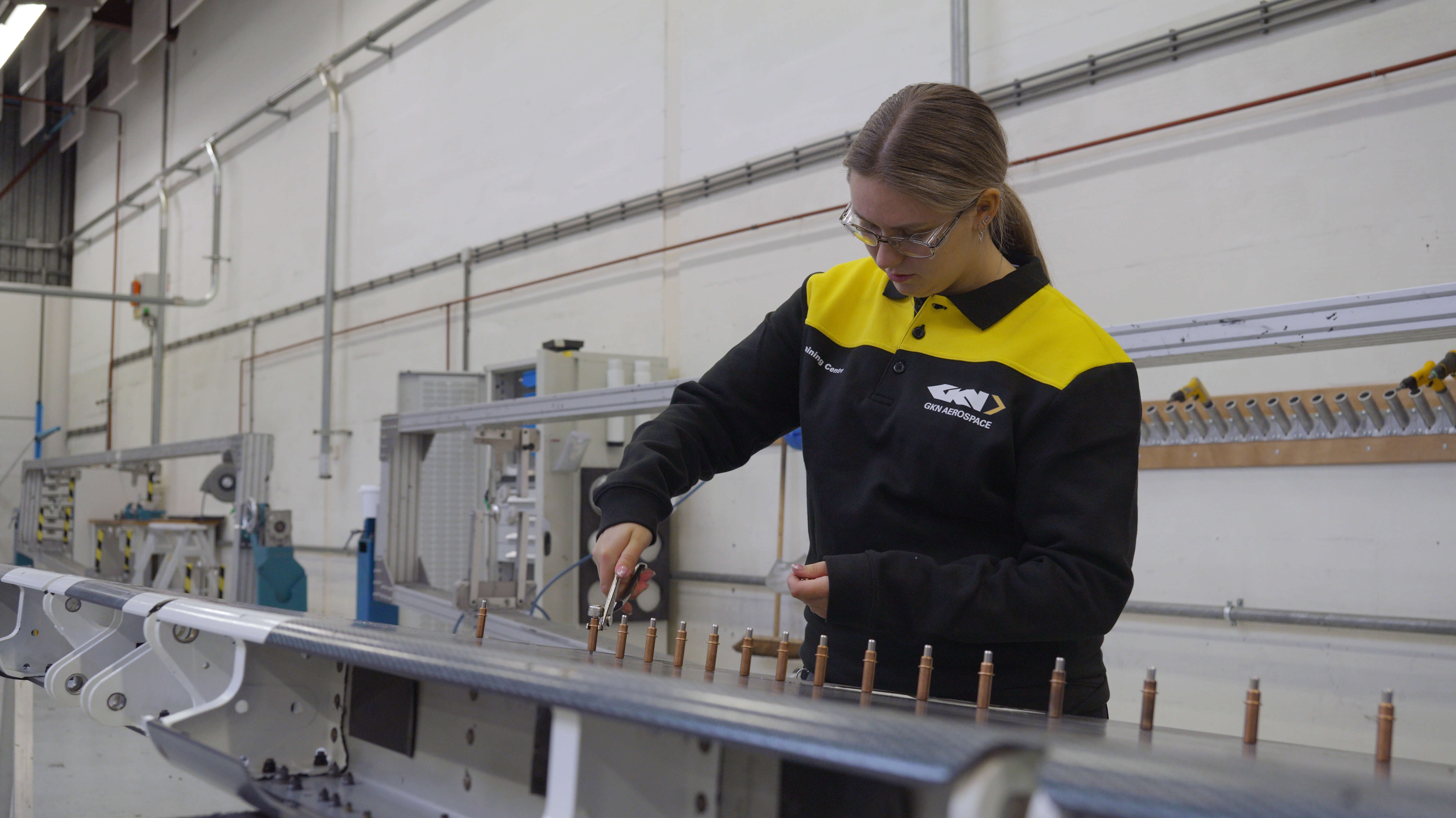Leerling werkt geconcentreerd aan luchtvaartonderdeel in een productieomgeving met precisiegereedschap