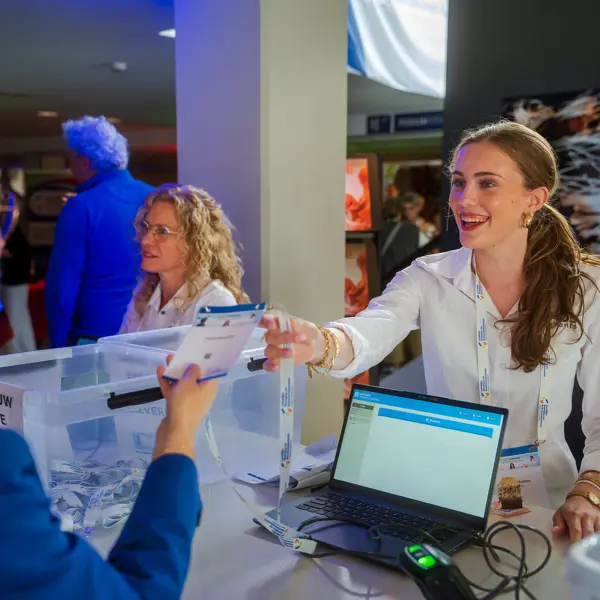 Medewerker evenementenorganisatie geeft bezoekers een toegangsbewijs bij inschrijfbalie tijdens een evenement