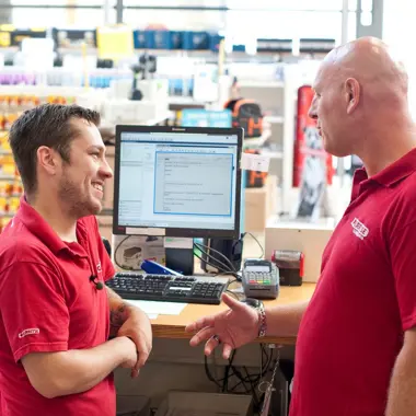 Commercieel medewerkers in gesprek bij balie met computer tijdens klantadvies en verkoopproces