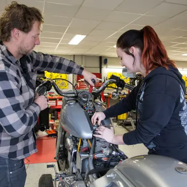 Technicus en student werken samen aan onderhoud van een motor in een praktijkwerkplaats mobiliteit en techniek