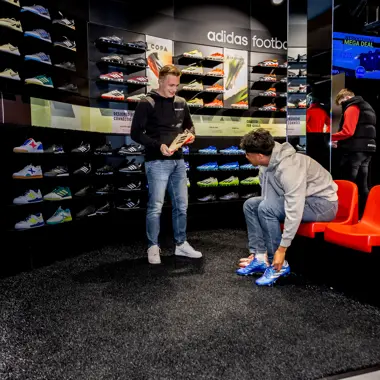 Consulent helpt klant met het uitzoeken van sportschoenen in een sportwinkel gespecialiseerd in voetbalartikelen