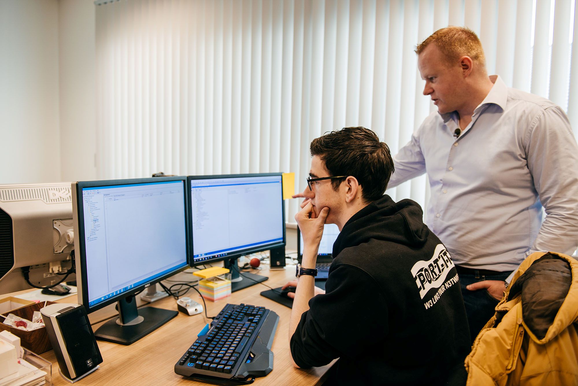 Student en docent werken samen aan het oplossen van technische problemen op een computer met meerdere beeldschermen.