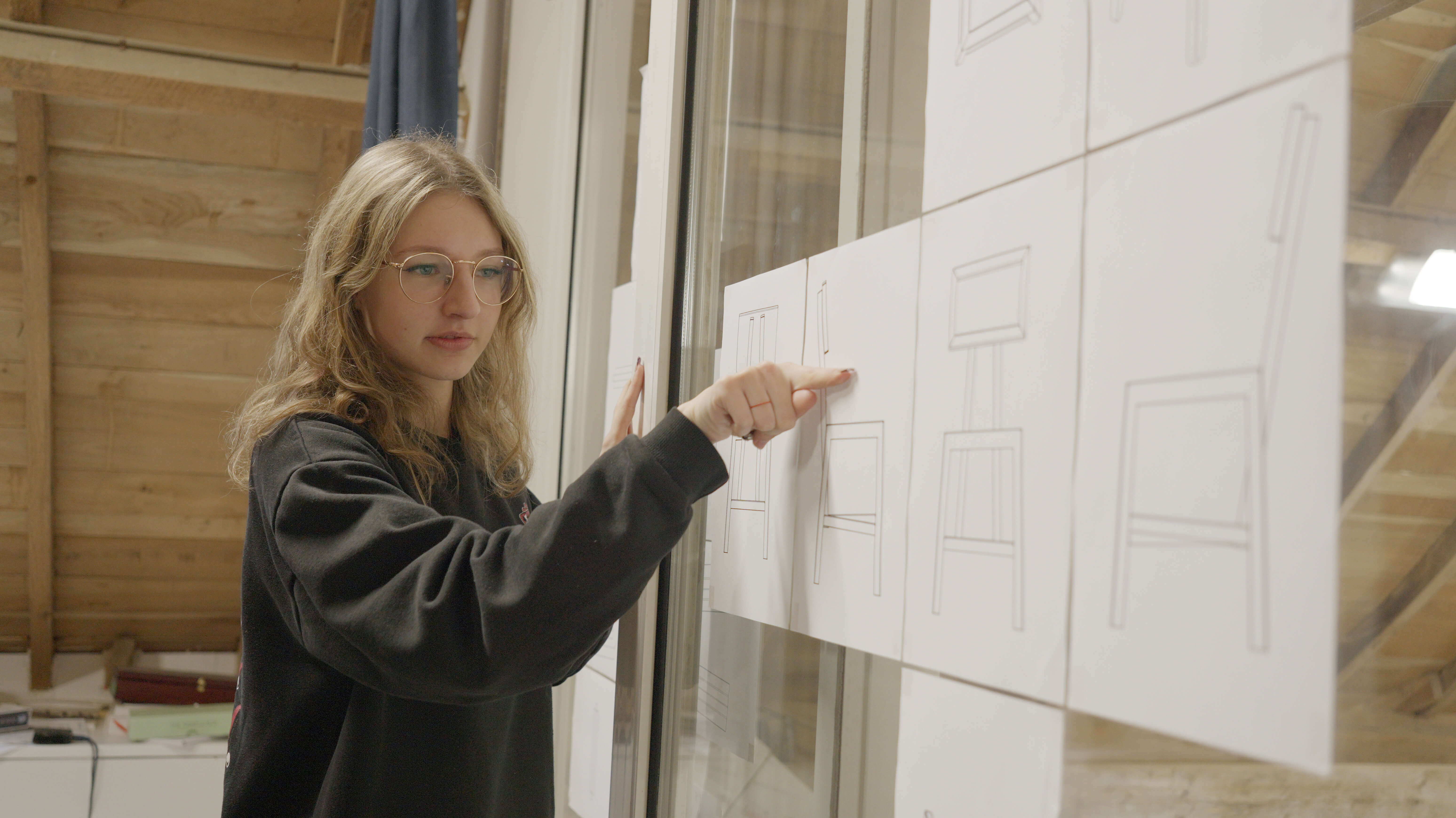Student onderzoekt bouwtekeningen van stoelen tijdens ontwerpstudie in een atelier