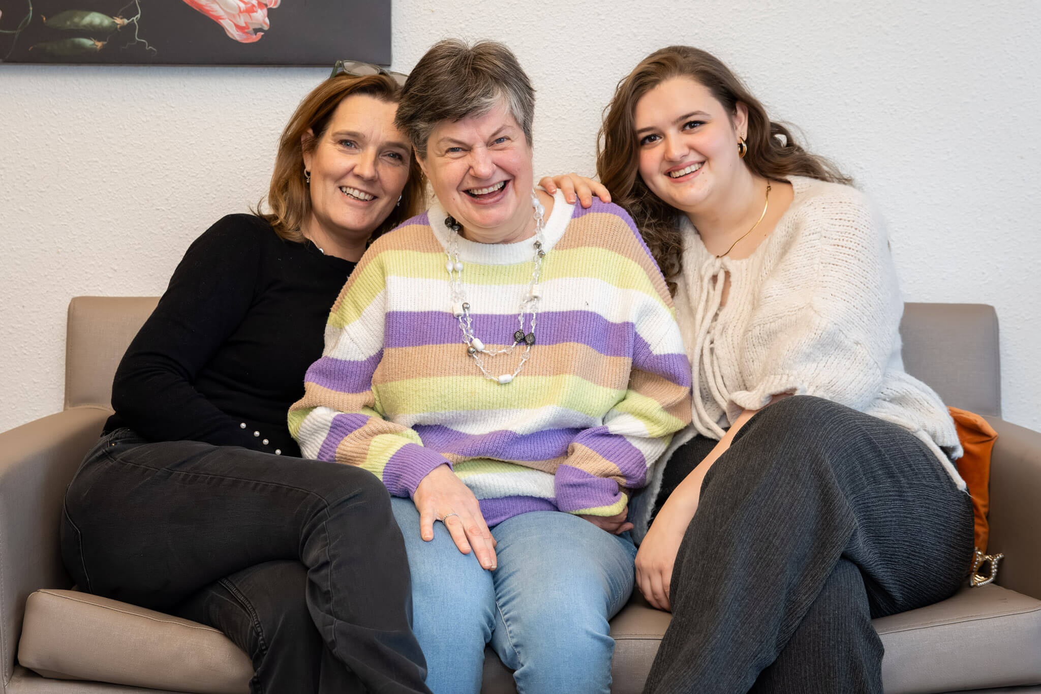 Drie personen samen op een bank, ontspannen en lachend tijdens een gesprek.