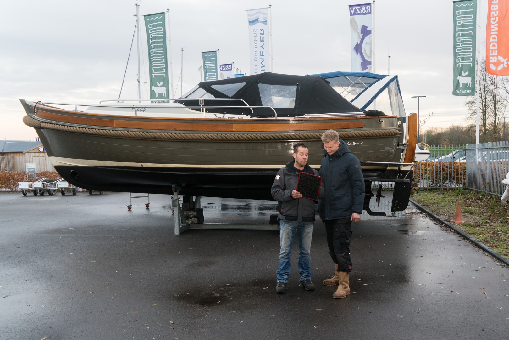 Twee medewerkers bespreken technische documenten bij een jacht dat op een werkterrein staat.