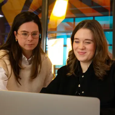 Twee studentes bespreken samen digitale media-inhoud op een laptop, gericht op communicatie en ontwerp.
