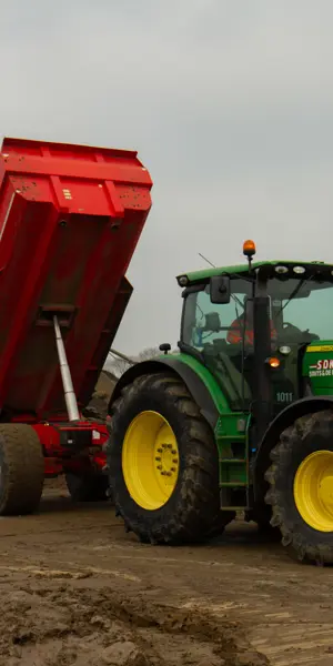 Groenmedewerker bedient landbouwvoertuig met kiepwagentje op bouwterrein voor grondwerkzaamheden