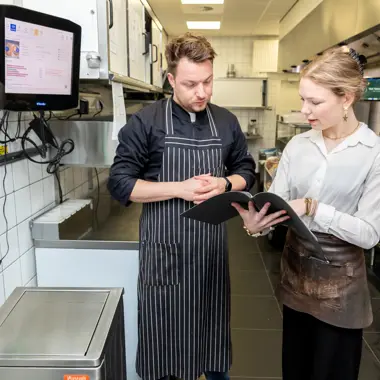 Twee medewerkers overleggen in een professionele keuken over de voorbereidingen voor de horeca.