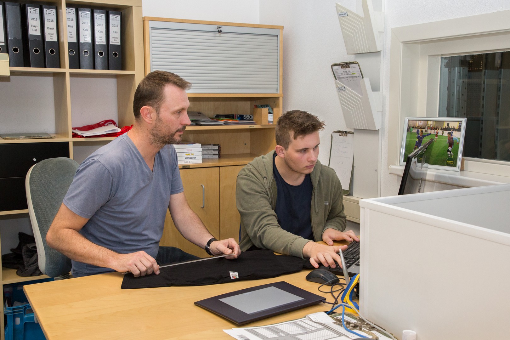 Twee studenten werken samen aan een ontwerp op een laptop in een klaslokaal voor media en vormgeving.