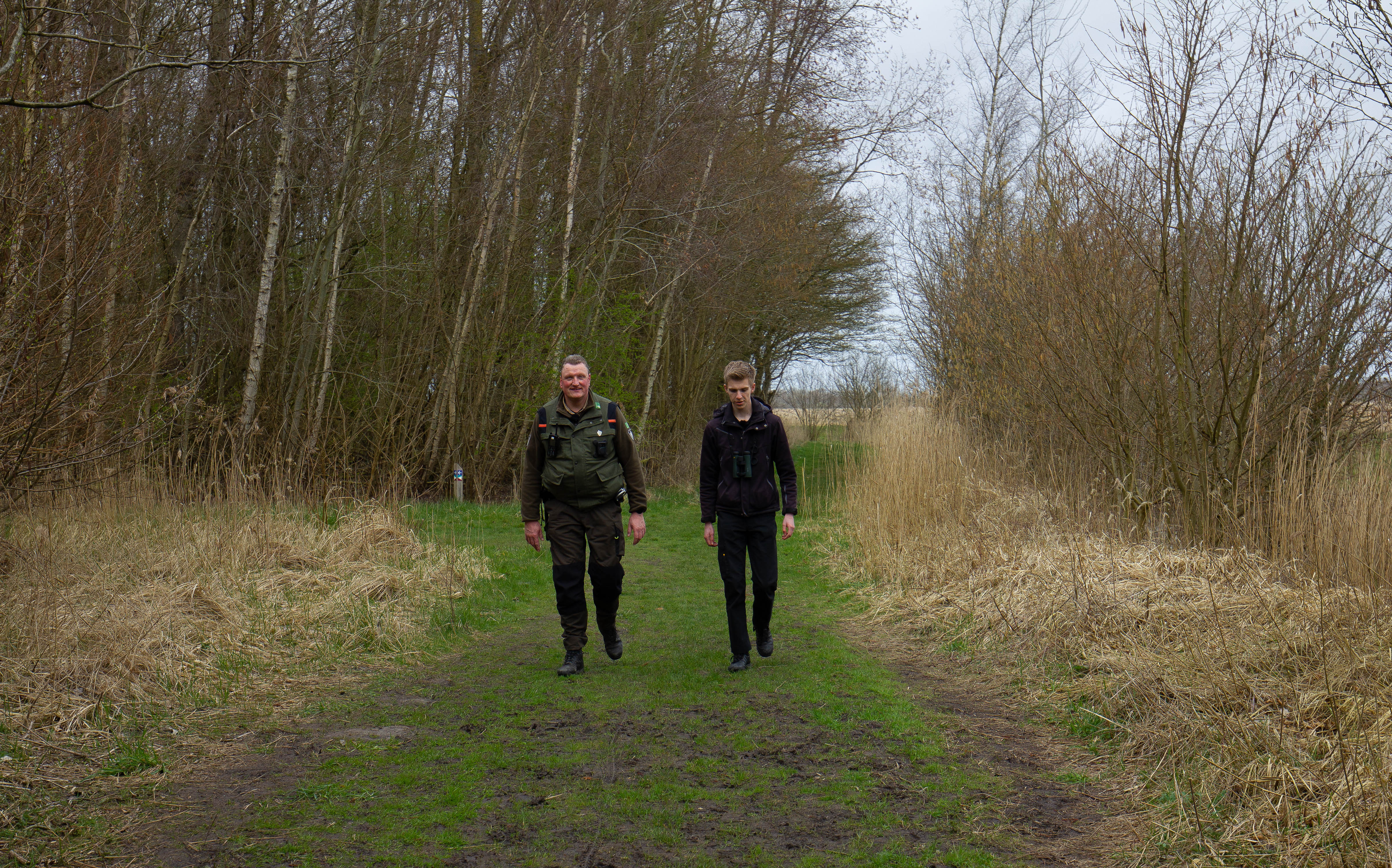 Twee handhavers lopen op een bospad en voeren toezicht en handhaving uit in een natuurlijke omgeving