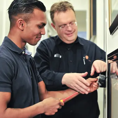 Twee onderhoudsmedewerkers werken samen aan een technisch paneel, gericht op installatie en reparatie.