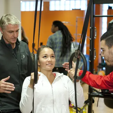 Sportbegeleiders ondersteunen een jonge sporter tijdens krachttraining in een sportschoolomgeving