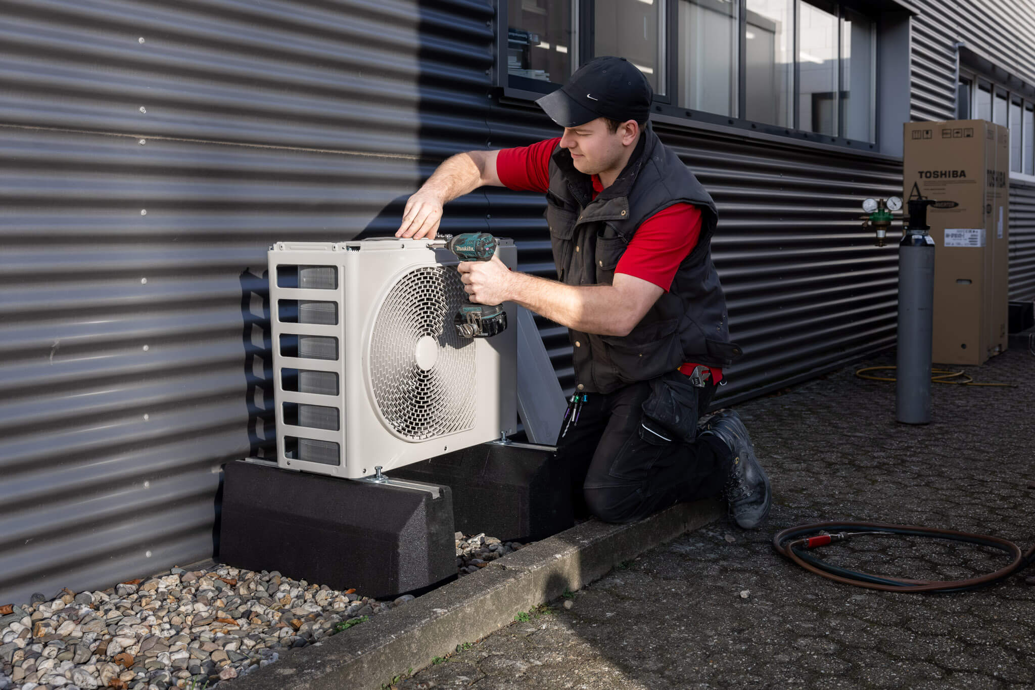 Technicus monteert een airconditioningsunit aan de buitenzijde van een gebouw.