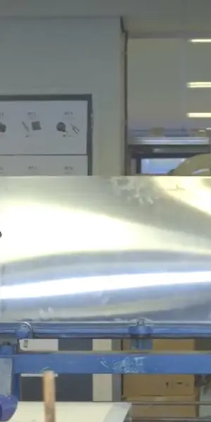 Twee monteurs werken samen om een groot metalen dakdeel te plaatsen in een werkplaats.