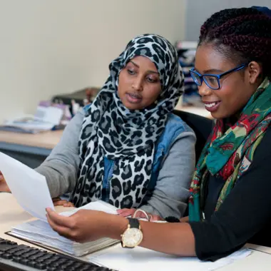 Twee medewerkers bekijken samen documenten en bespreken kantoorwerk in een administratieve omgeving.