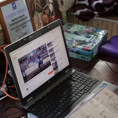 Laptop met video over paardenverzorging op bureaublad met documenten en muis ernaast