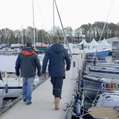 Twee studenten lopen op een steiger tussen zeilboten, werkend aan vaardigheden voor de maritieme techniek.