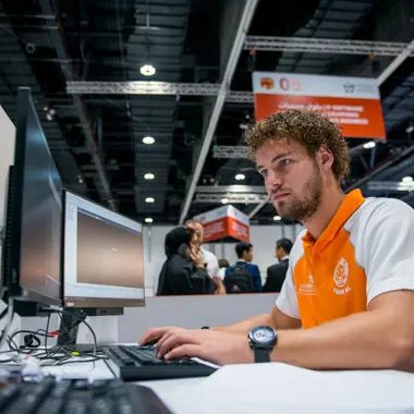 Student werkt geconcentreerd aan een commercieel project op computer bij een onderwijsbeurs