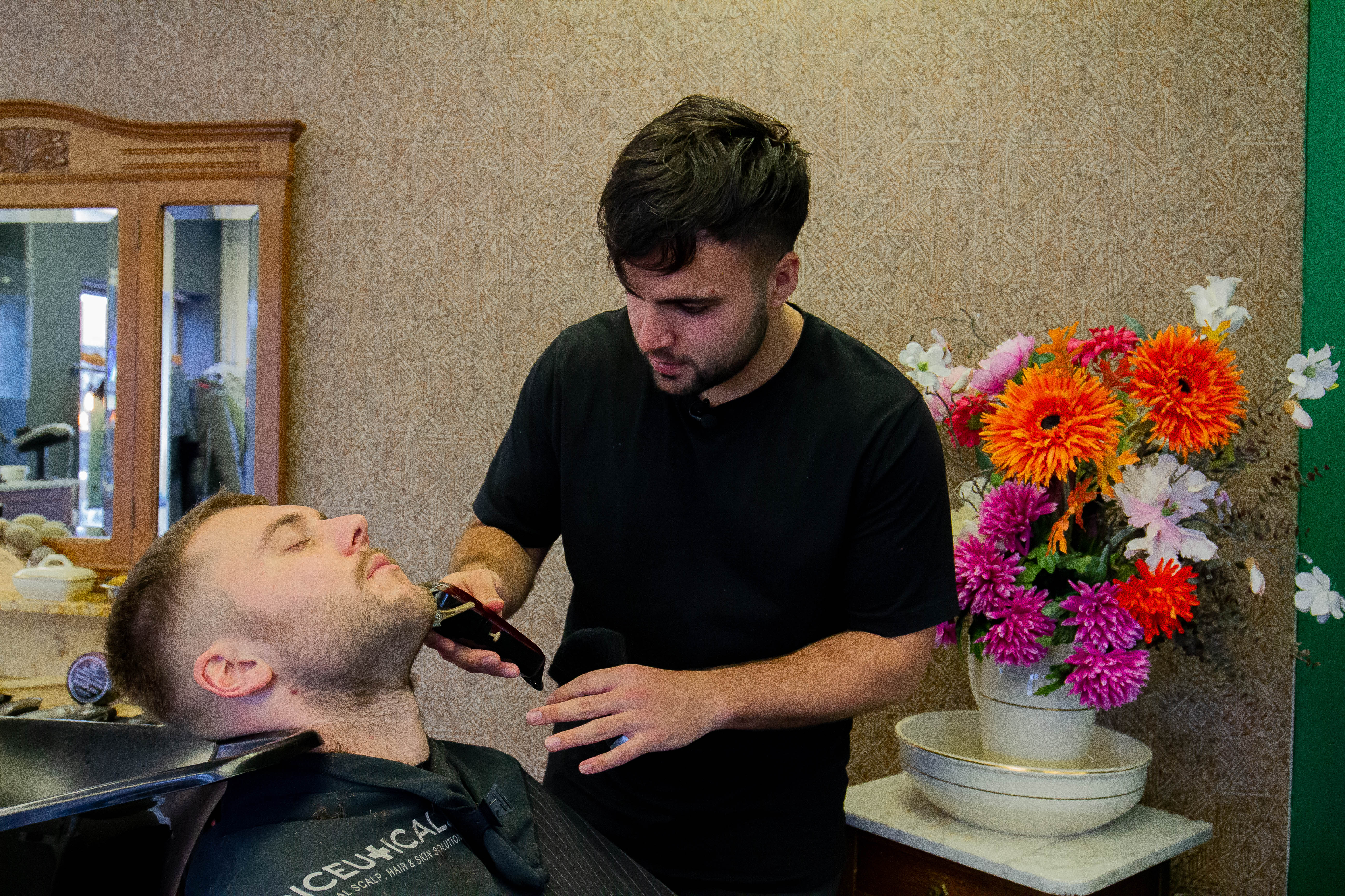 Een leerling haarstylist verzorgt het knippen van een baard tijdens praktijkles in een kapsalon.